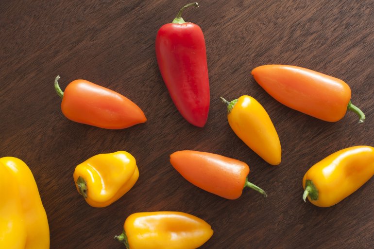 Whole red and yellow peppers on dark brown wooden background, viewed from above