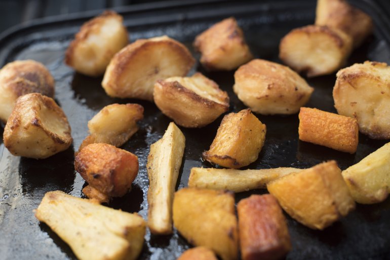 Roasting slices of potato and parsnips on a pan, viewed in close-up from high angle