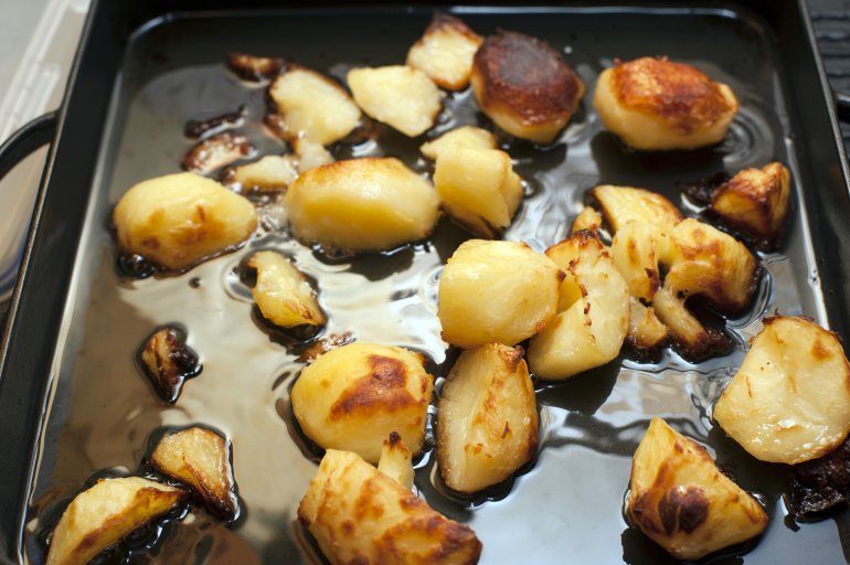 Golden crisp roast diced potatoes on an oily oven grilling pan ready to be served for dinner, close up high angle view