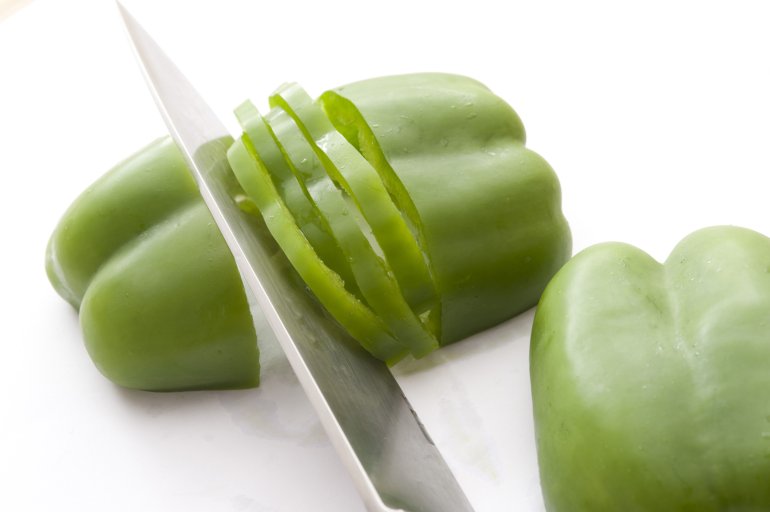 Cut green pepper with knife on white background