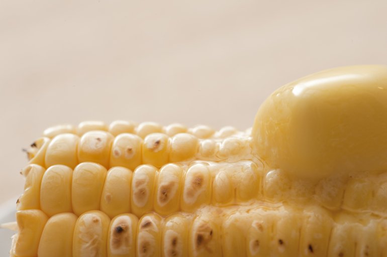 Hot grilled sweet corn with a dollop of melting butter, close up view of the kernels and butter over a neutral beige background with copyspace