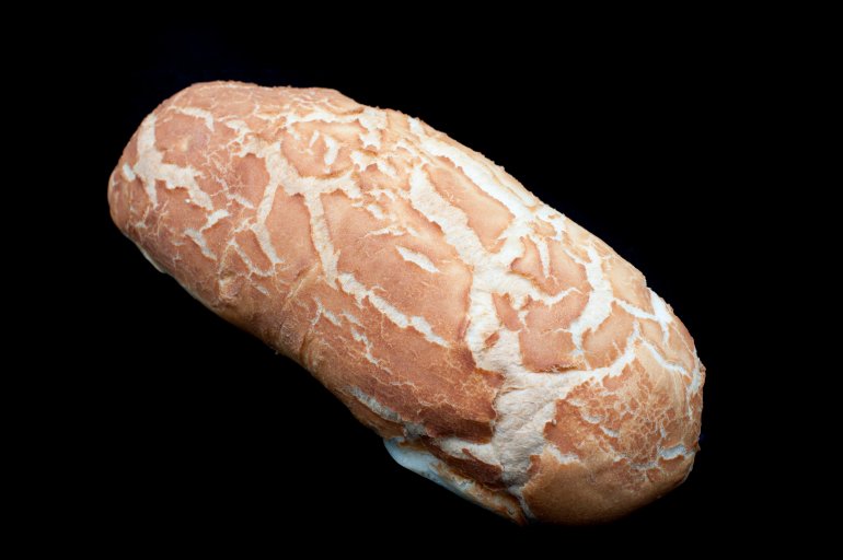 Whole crisp crusty loaf of freshly baked white bread on a black background