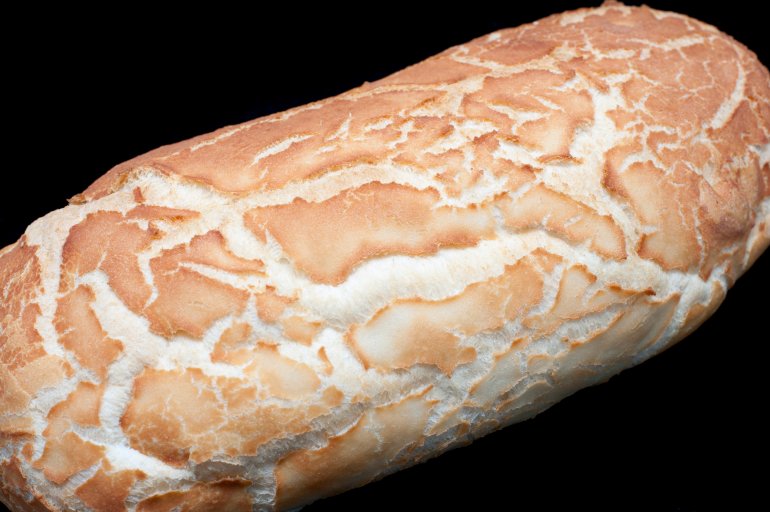 Overhead view of a crisp loaf of batard bread which is similar to a baguette on a dark background