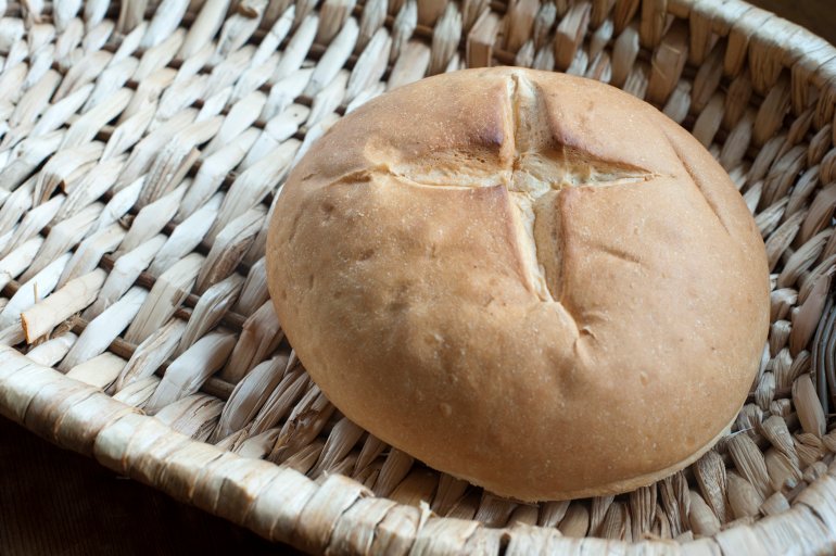Round crusty cob loaf, a traditional bread with an incised cross, on a wicker basket with copyspace
