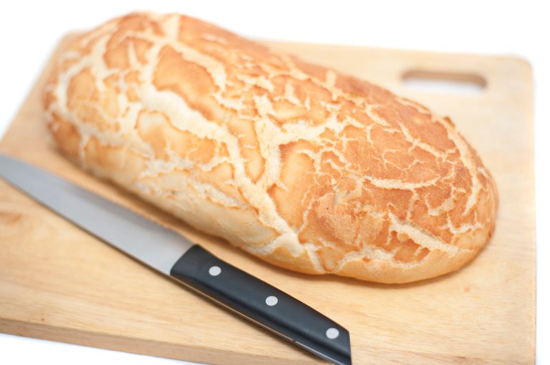 Freshly baked uncut loaf of crusty white bread on a bread board with a bread knife isolated on white
