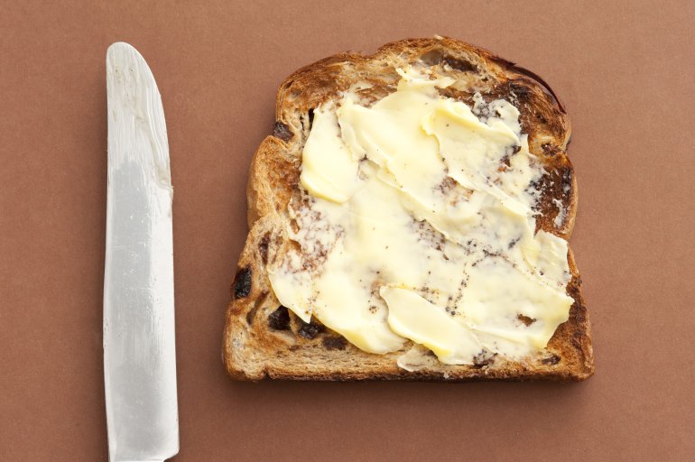 Close-up of delicious slice of bread with spreading butter and knife on brown background. From above