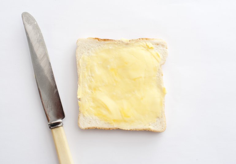 Isolated slice of white bread with butter and knife on white background. From above
