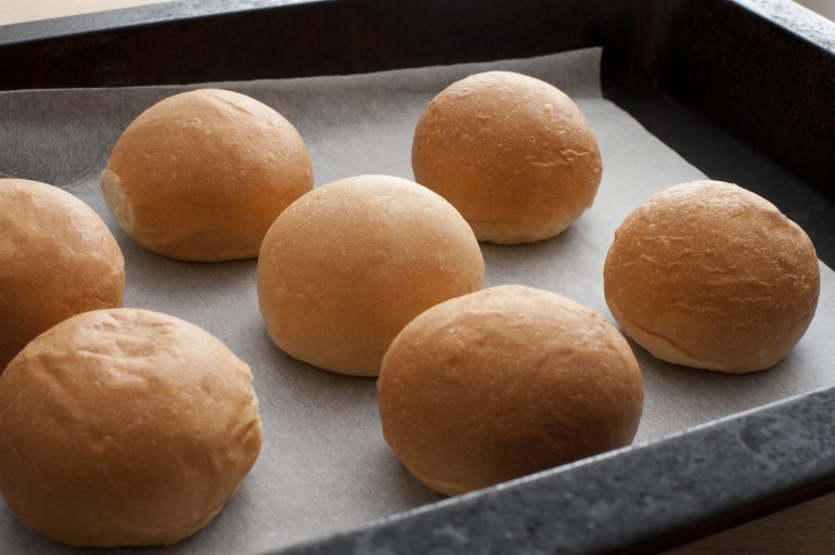 Batch of freshly baked crusty bread rolls on oven paper in a baking tray for an appetiser or accompaniment to dinner, close up high angle view