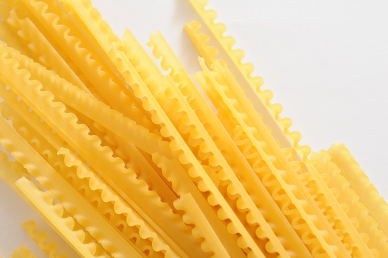 Dried reginette Italian pasta with its frilled wavy edges on a white background, overhead view with copyspace