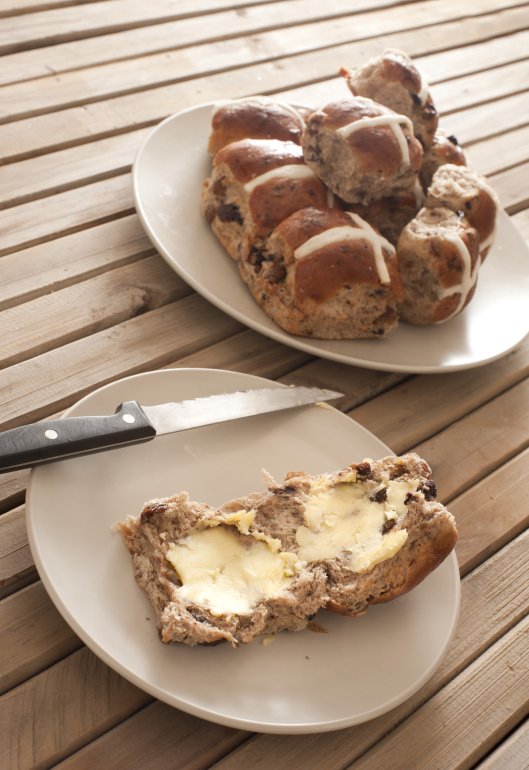 Close-up of several buns on plates and knife. One covered with butter. Daylight