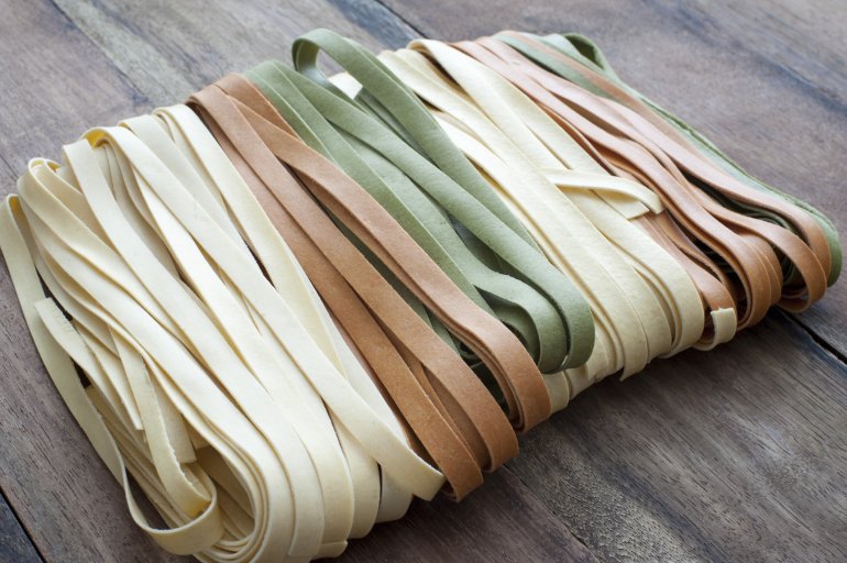 Photo of beige, orange and green fettuccini on wooden table. Daylight
