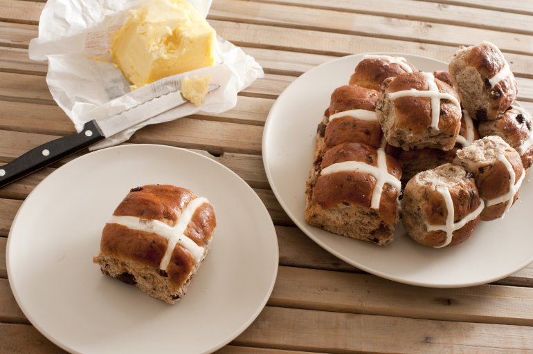 Batch of freshly baked hot cross buns with a single bun on a plate and pat of farm butter, high angle view