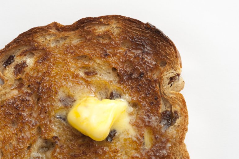 Dollop of melted fresh farm butter on a hot slice of toast with raisins viewed close up from above over white
