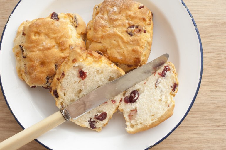 Sliced freshly baked bread scone with fruity raisins on a plate with two uncut scones, overhead view with a knife