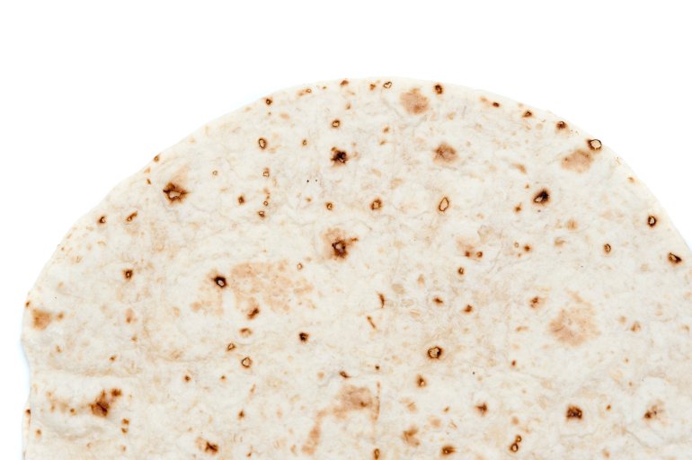 overhead partial view of a tortilla which is a thin disk of unleavened bread made wheat flour and baked on a hot surface, isolated on white