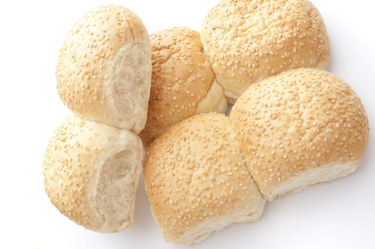 Batch of fresh joined sesame rolls from a bakery with two broken off to show the texture of the bread viewed overhead on white