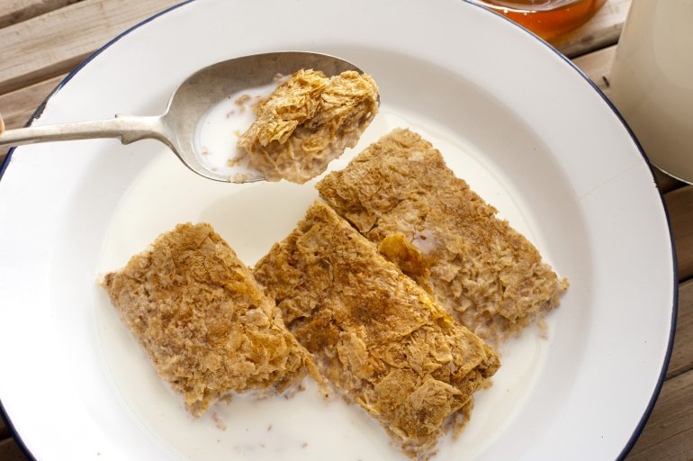Wholewheat breakfast cereal rich in dietary fibre served with milk in a bowl with a mouthful raised in a spoon for selective focus, overhead view