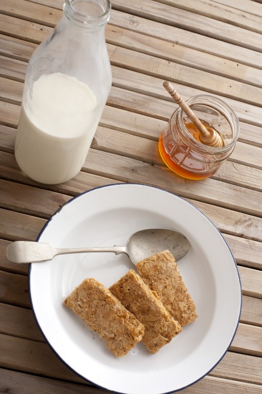 First person perspective view on whole wheat cereal crackers with honey, dipper and large glass jar filled with milk on table with smooth planks of wood