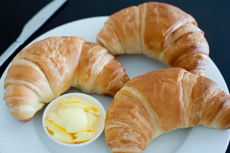 Crispy freshly baked golden croissants and butter served on a plate for a delicious breakfast or snack