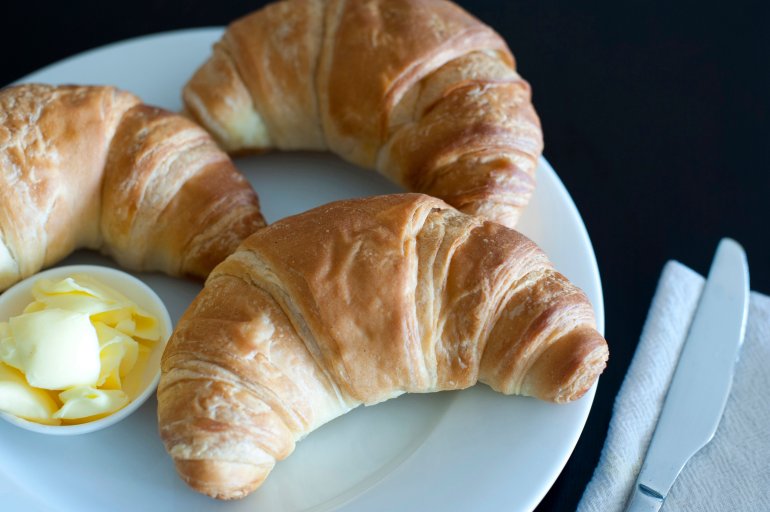 Overhead view of three golden crisp flaky fresh croissants served with butter on a plate for breakfast