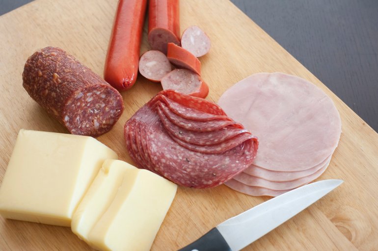 German breakfast with sliced spicy salami, ham, sausages and portions of cheese being prepared on a wooden chopping board with a knife