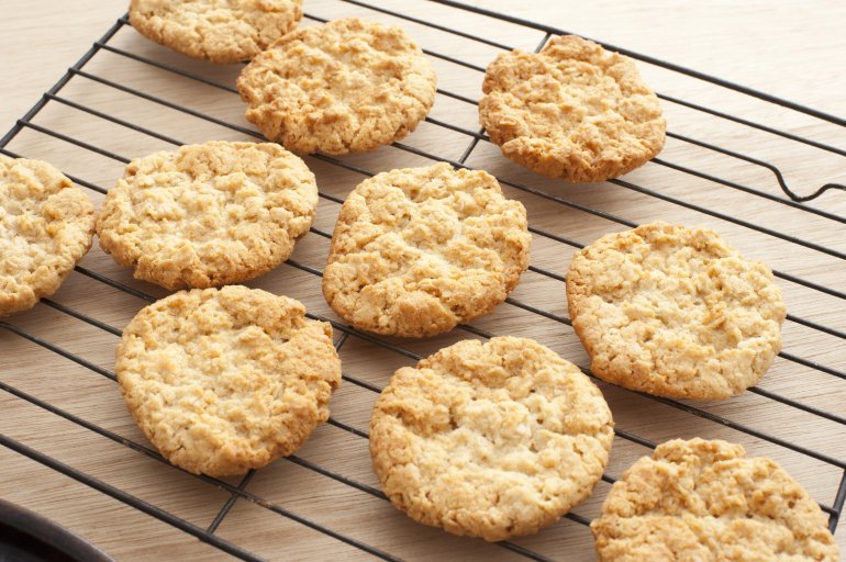 Cropped view on ten delicious freshly baked anzac cookie biscuits on slotted oven tray over wooden table