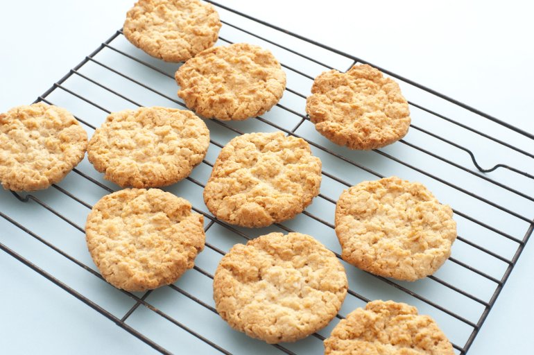 Freshly baked crispy golden oat cookies cooling on a wire rack in the kitchen after removal from the oven, high angle view on white