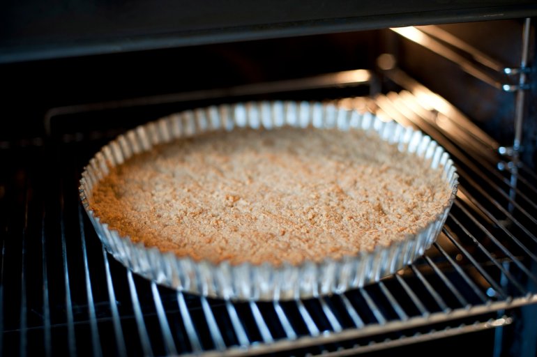 Cake base cooking in the oven in a decorative fluted round metal pie pan viewed under the interior light of the oven
