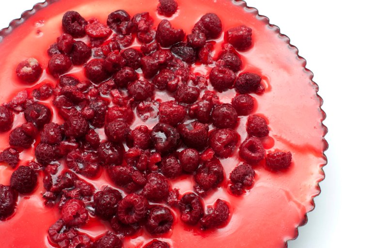View from above of a freshly baked cheesecake in a fluted pan topped with tasty raspberries for a gourmet dessert