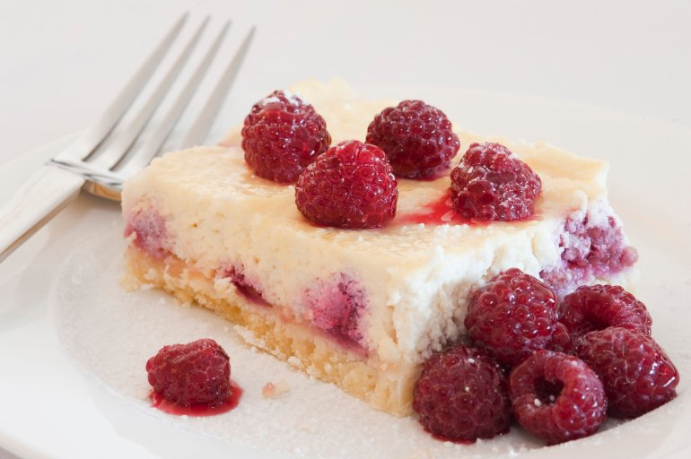 Portion of freshly baked ricotta cheesecake dessert topped with raspberries served with a fork