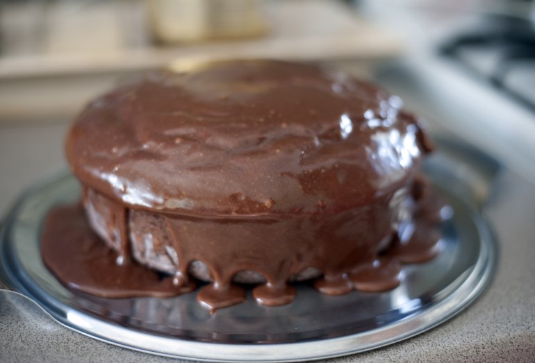 Selective focus close up on round chocolate cake recently coated with icing dripping from the sides on steel pan