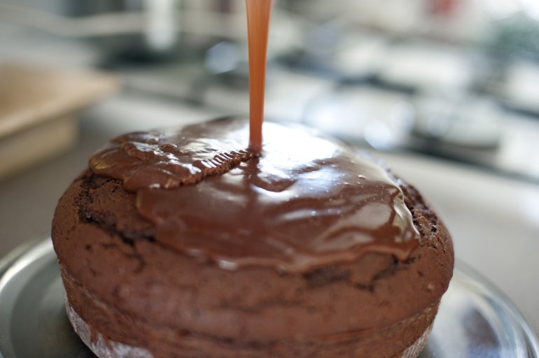 Selective focus view of top center section of chocolate cake with stream of delicious icing being poured on top of it