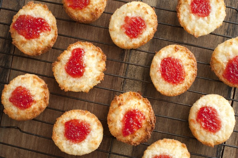 Tasty home baked coconut drop cookies topped with colorful red strawberry jam cooling on a wire rack in a kitchen, overhead view
