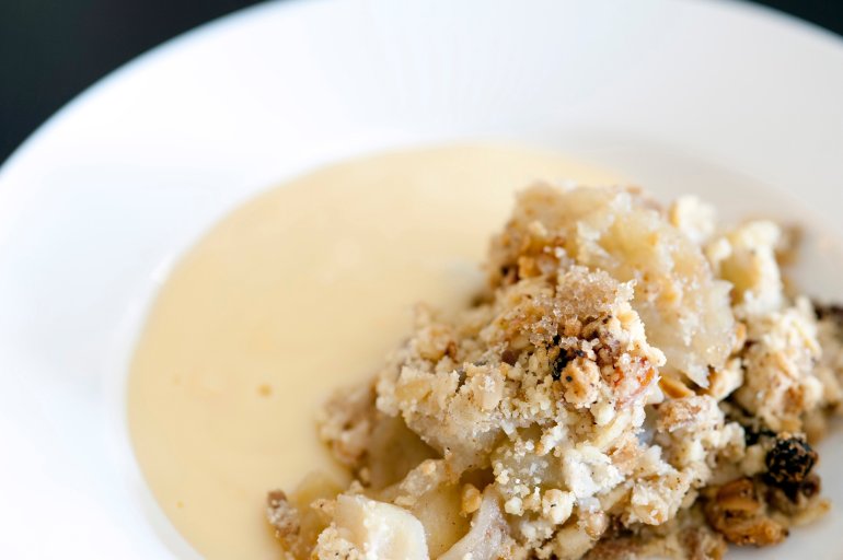 Plate of delicious baked apple crumble and custard with a spicy topping using cinnamon and raisins, closeup view
