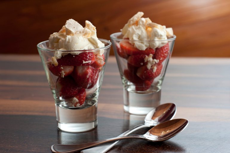 Fresh ripe red strawberry and cream dessert served in glasses and standing on a wooden counter top with two spoons