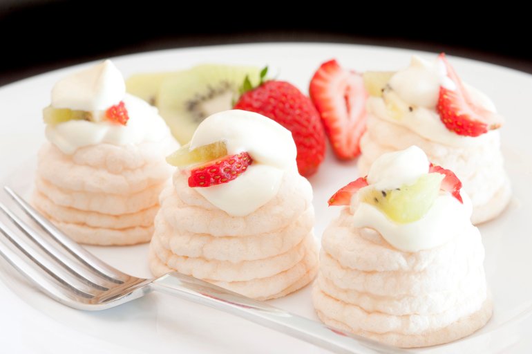Individual meringue cases filled with whipped cream and topped with sliced fresh fruit including strawberries and kiwi fruit