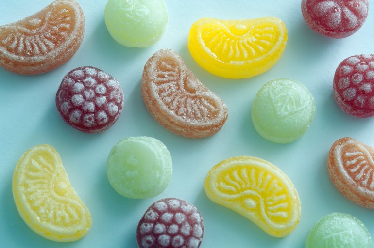 Lemon, lime, orange and raspberry shaped flavored candy pieces spaced out over green background