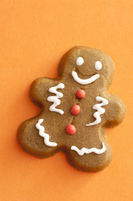 Gingerbread man or cookie decorated with icing on a festive orange background with copy space, overhead view