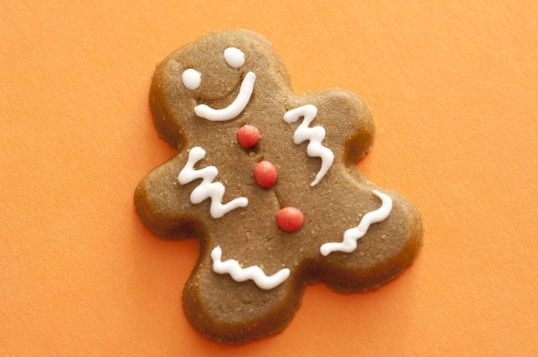 Festive decorated gingerbread man with icing accents on a colorful orange background, close up view with copy space