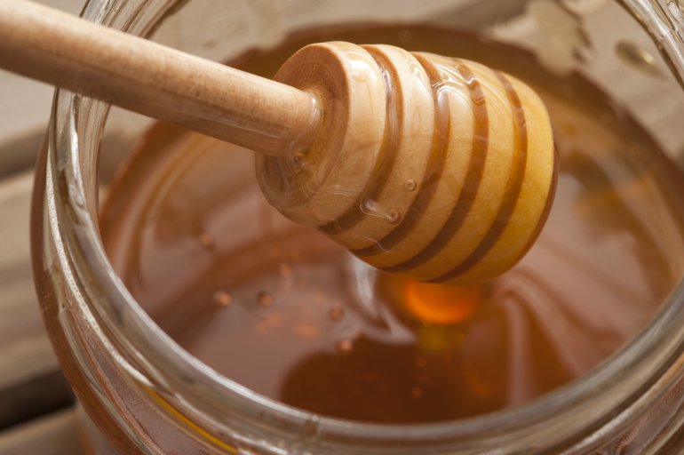 Close up of ribbed wooden dipper in large glass jar filled up with sweet yellow honey