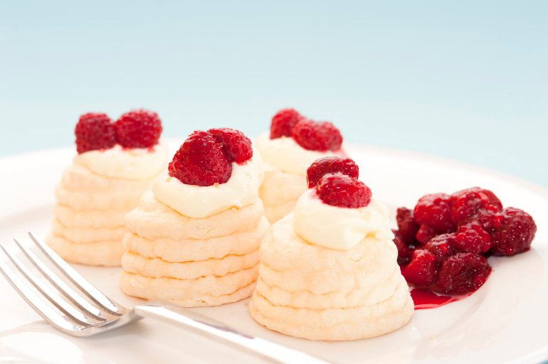 Decorative twirled meringues filled with whipped cream and topped with fresh raspberries served on a plate with a fork