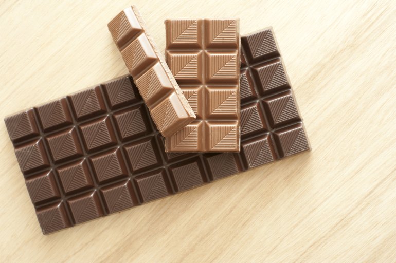 Bars of milk and dark chocolate candy unwrapped and displayed on a wooden table with copy space viewed from above