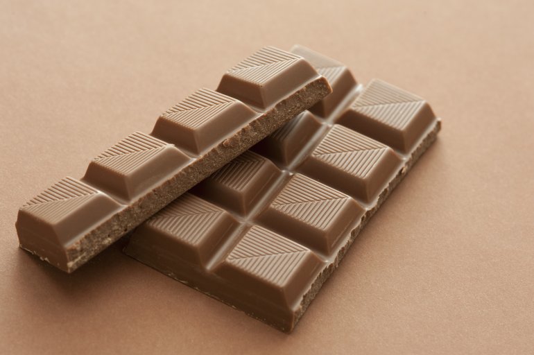 Squares of milk chocolate from a candy bar with a decorative striped pattern on a light brown background with copy space