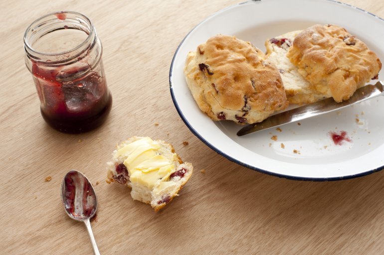 Scrumptious sliced breakfast scones with butter and strawberry jelly jam on plate over wooden table