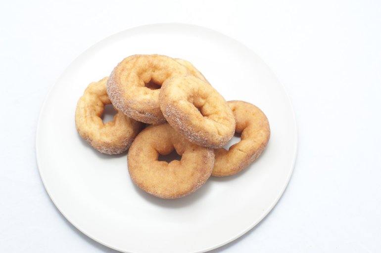 Plate of five sweet plain ring doughnuts for a tasty but unhealthy snack or breakfast viewed high angle on white