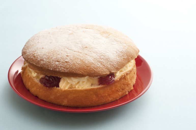 Delicious single little round victoria sandwich sponge cake filled with cream and fruit on red plate over white table