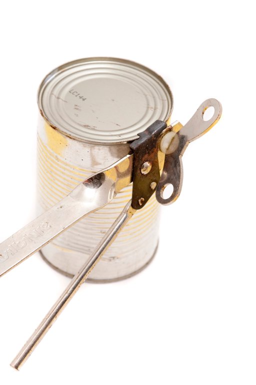 Opening canned vegetables with a manual steel can opener over a white background, close up view of an unlabelled can