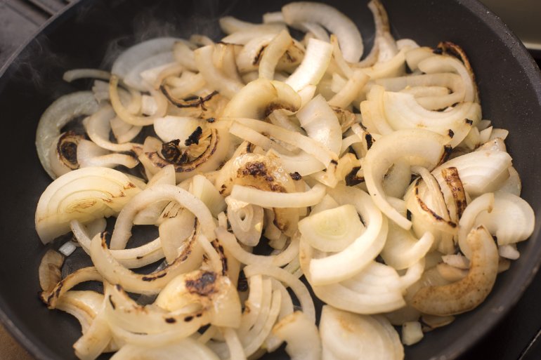 sliced fresh white onions browning in a frying pan in a close up high angle view