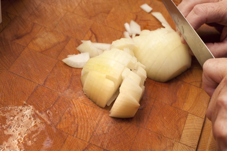 Left handed chef dicing onion on a kitchen counter preparing it for cooking , close up of the blade and his hands with copy space