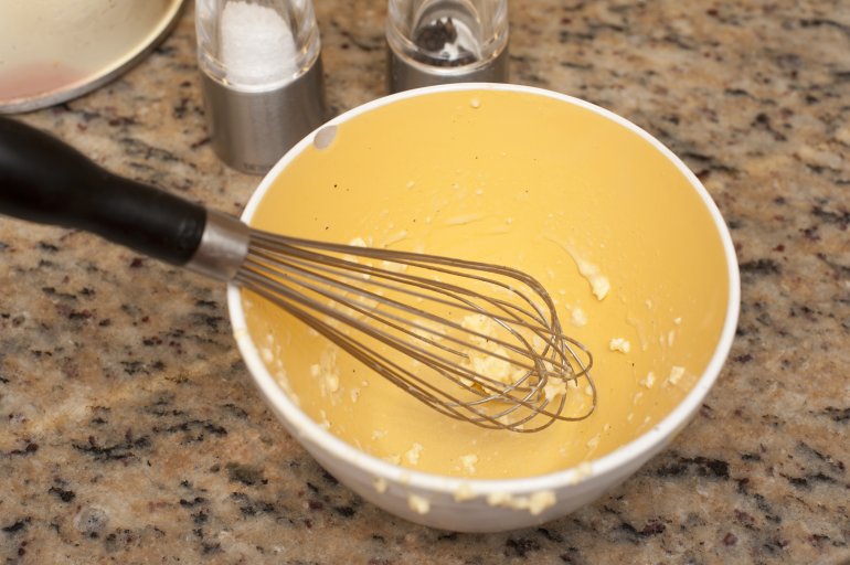 Empty mixing bowl with remnants of batter and a manual wire whisk on a granite kitchen counter in a baking concept